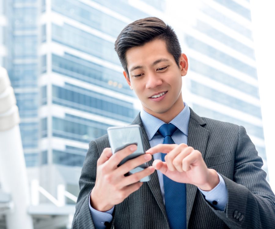 Image depicting a business man standing outside a high-rise building interacting with his mobile phone