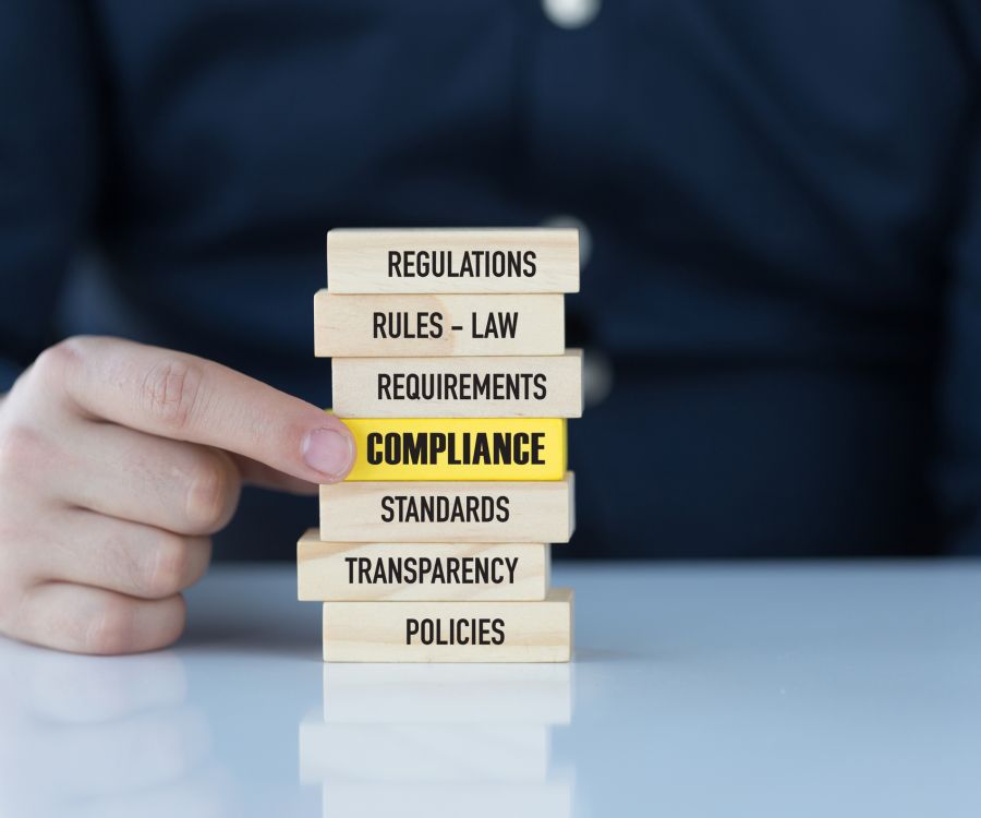 A stack of wooden blocks showing business and legal terms with the word, "Compliance", highlighted in yellow.