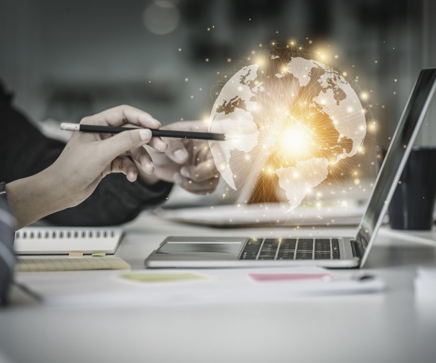 A futuristic image of two people working together on a laptop, with a glowing globe hovering above it.