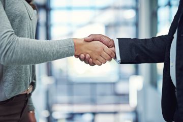 Cropped image of man and woman in bright business environment shaking hands