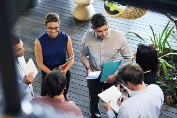 Image taken above a group of business people holding documents who are outside in a huddle meeting