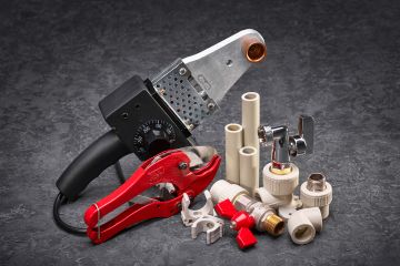 Image of  a collection of plumbing tools and components, including a pipe cutter, a heat welding machine, plastic pipes, fittings, and valves.