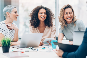 Four women in a business meeting engaging in friendly conversation