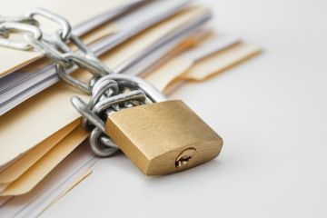 A stack of documents is secured with a heavy chain and locked with a brass padlock, symbolising data security or restricted access.