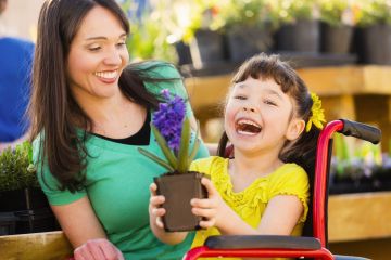 Young carer helping a wheelchair bound girl work with beautiful purple potted plant. Both are smiling and happy.