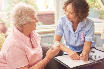 Image of female carer leaning in to care for an elderly resident or patient. She is intent on the patient's needs.