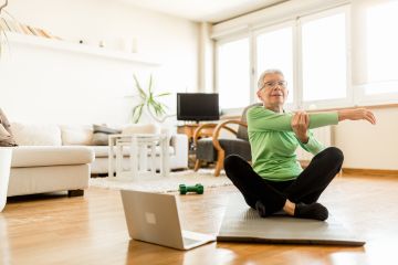 Contemporary elderly woman sitting on an exercise mat stretching in lieu of doing or having completed an online workout