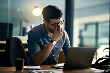 Stressed business man sitting at his lap top cradling nose in his fingers 