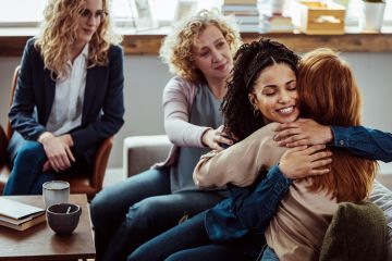 A group of women shares a moment of emotional support, with one offering a warm hug while others provide comfort and understanding.