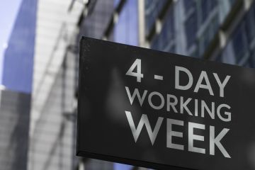 Image of a suspended street sign in the city saying, "Four day Week".